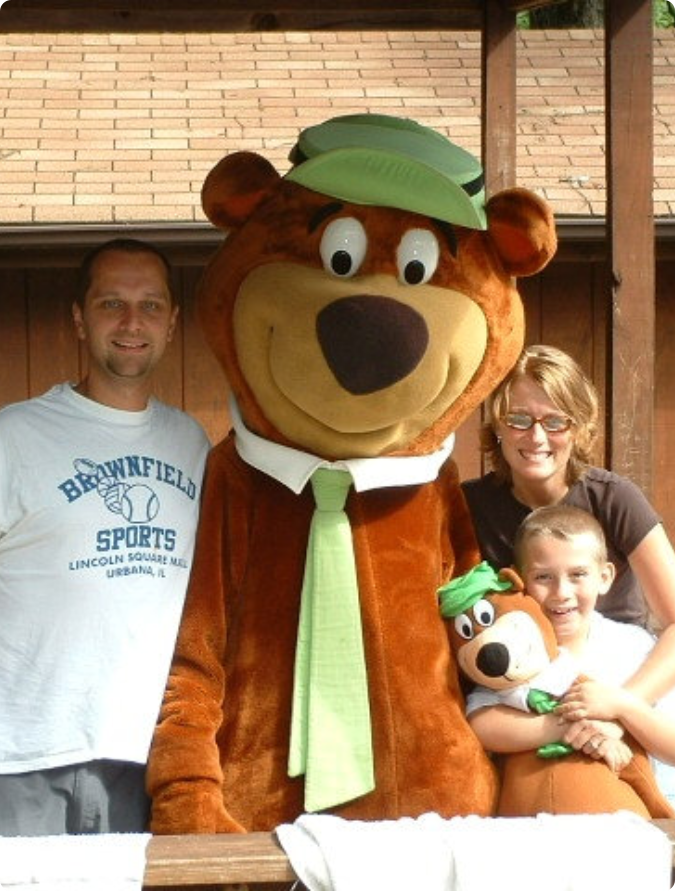 A family smiles while posing with a friendly bear mascot