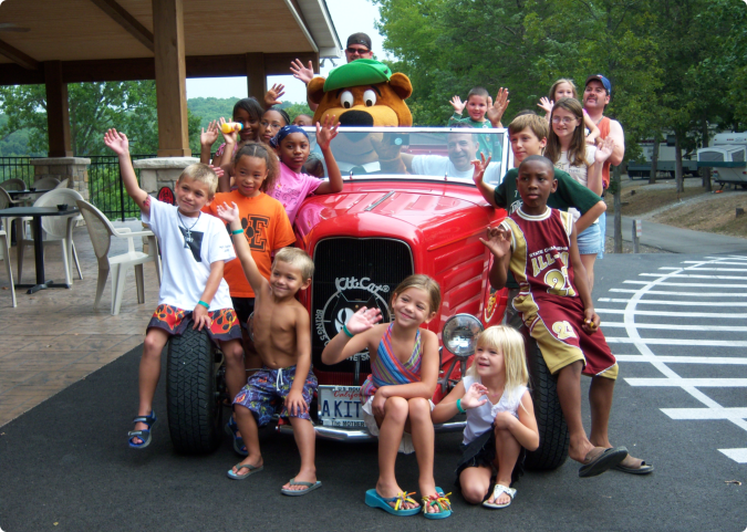 A group of children smiling and posing together in front of a parked car