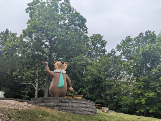 A bear statue wearing a green hat stands in a park