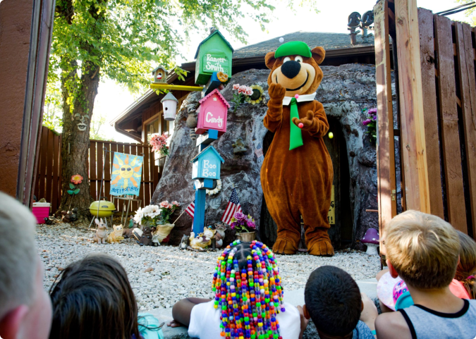 A bear mascot sits in front of a group of excited children
