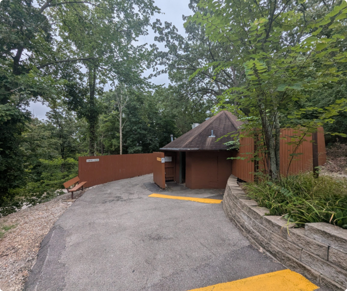 A small building with a yellow stripe beside a bear mascot roasting marshmallows over a campfire.