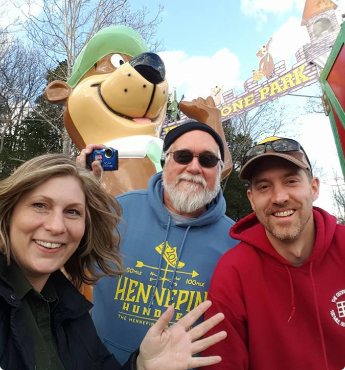 Three people smile while posing next to a large bear statue