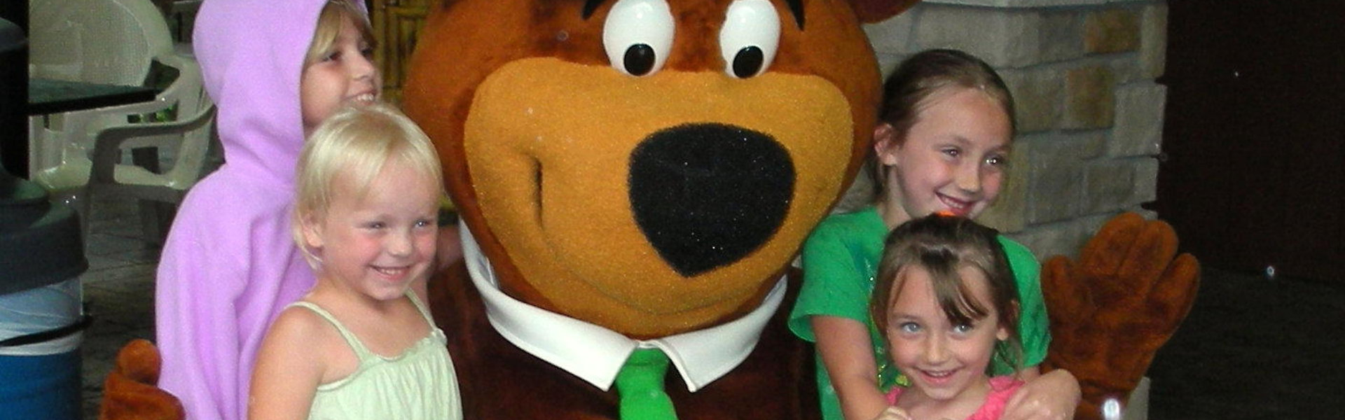 Children happily gather around a large bear mascot,