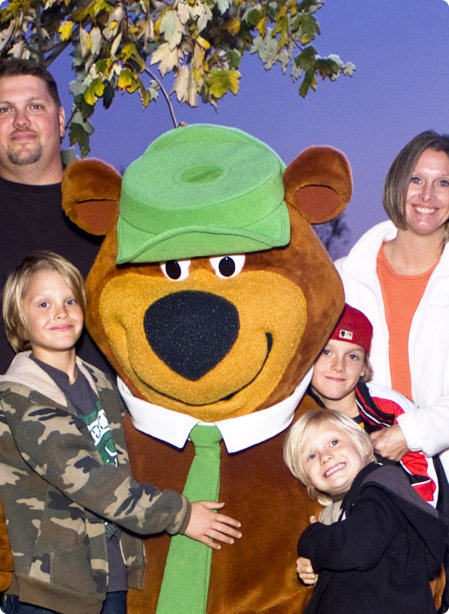 A family smiles and poses together with a large bear mascot